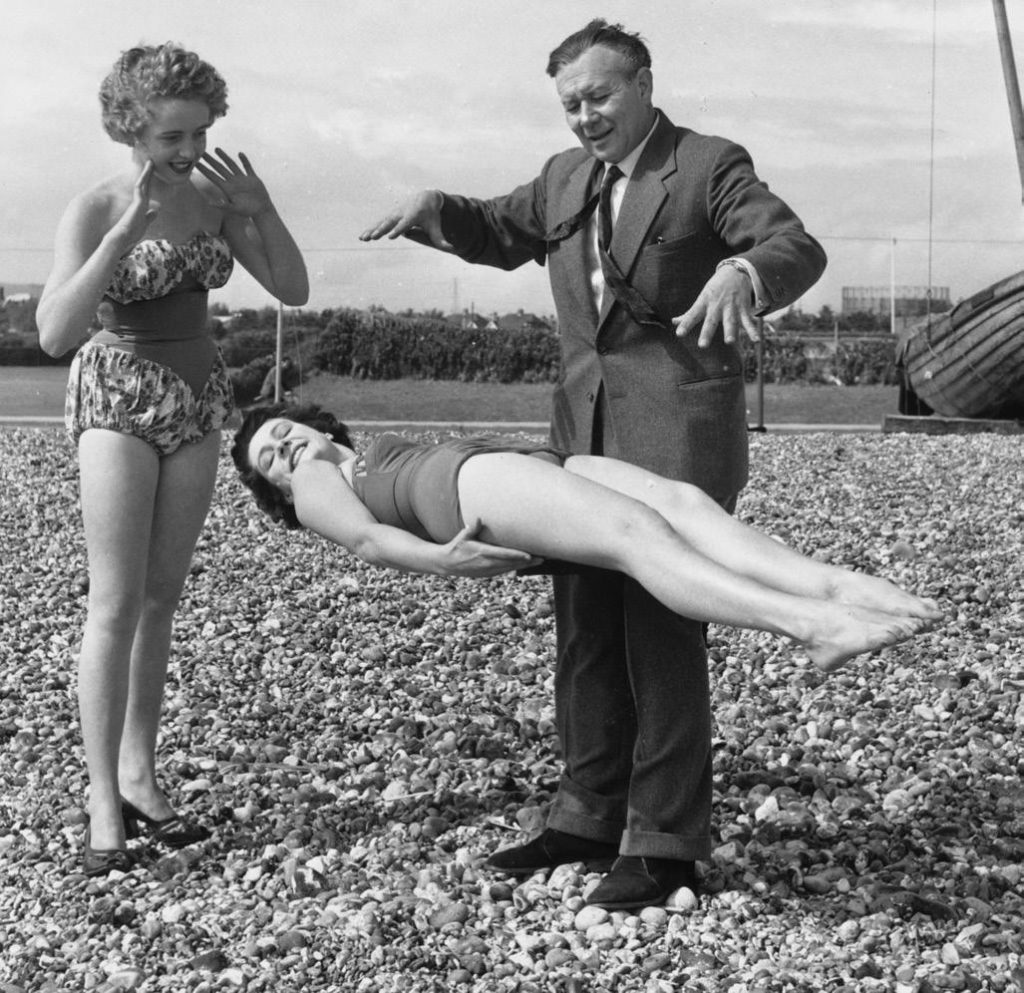 Magician Robert Harbin demonstrates one of his levitation tricks to a couple of sunbathers on the beach at Eastbourne.